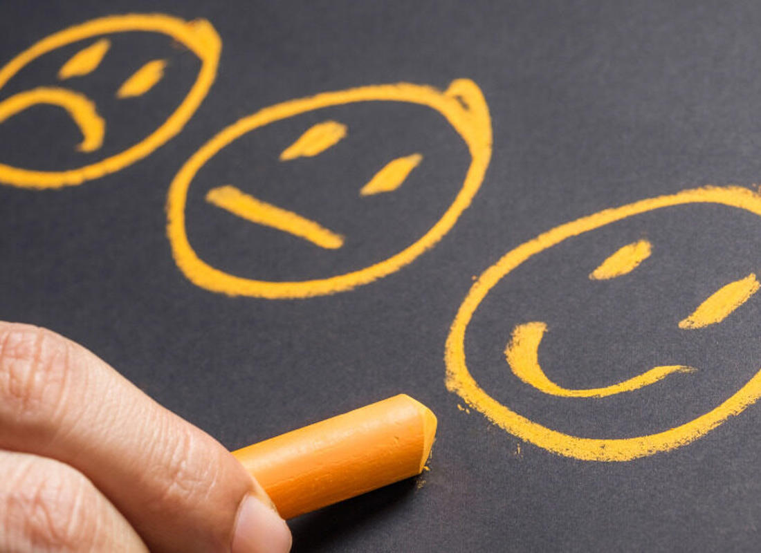 three ai generated smiley faces drawn on a blackboard by a hand holding chalk