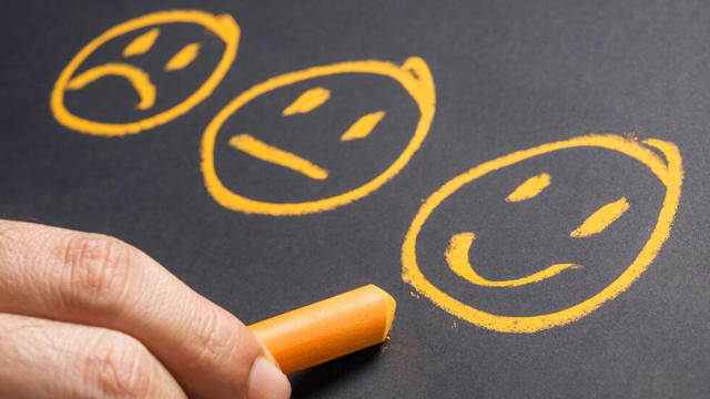 three ai generated smiley faces drawn on a blackboard by a hand holding chalk