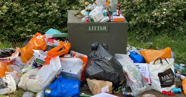 a pile of rubbish and litter surrounding a litter bin in a park