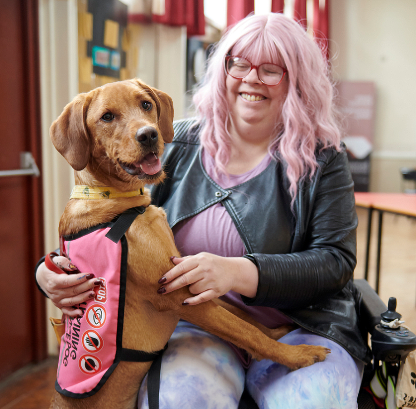 Resident using a wheelchair with an assistance dog at a community event.
