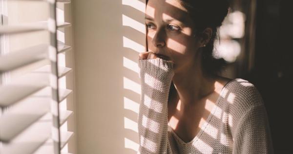 a worried looking woman peeking through a window with the blinds down