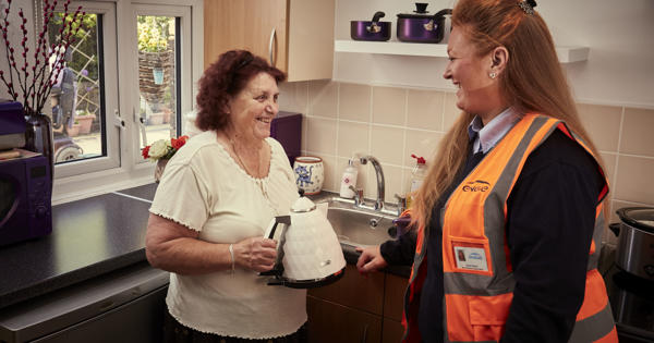 an elderly resident in her kitchen, holding a kettle and talking to an engie engineer