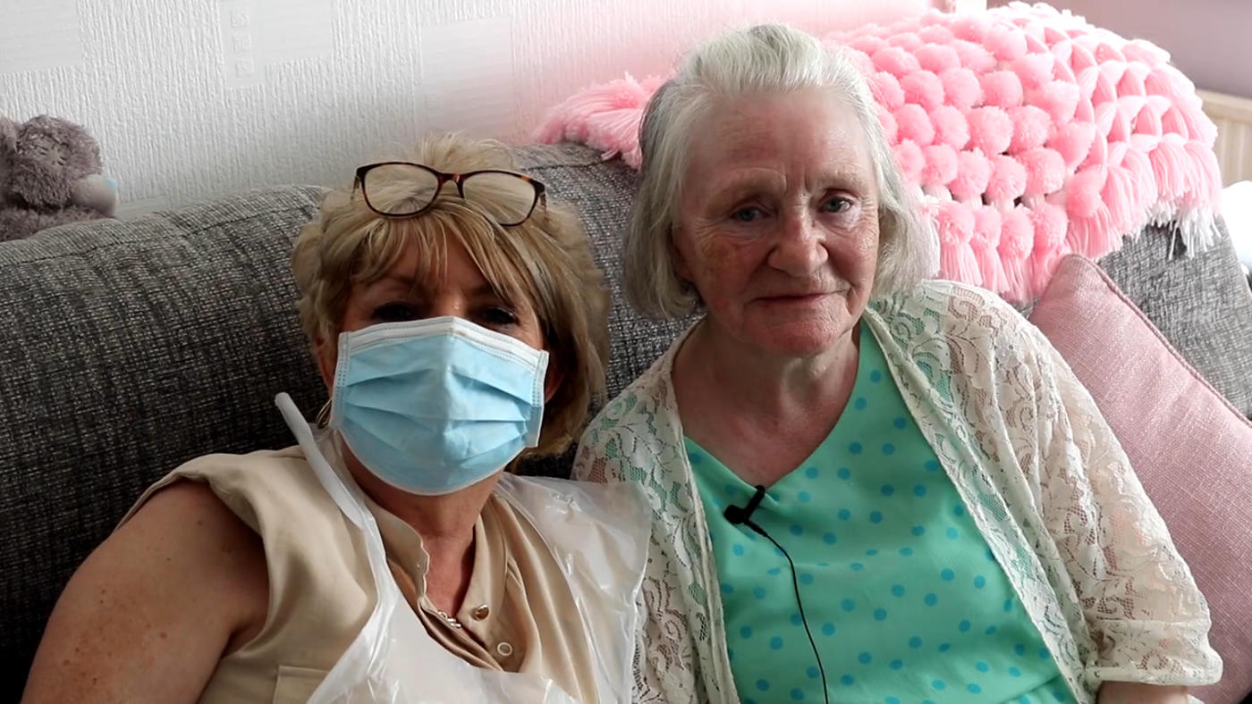 two residents sat on their sofa, one wearing COVID PPE