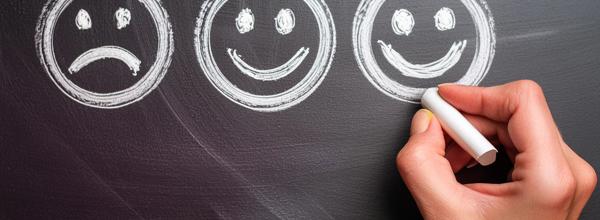 three ai generated smiley faces drawn on a blackboard by a hand holding chalk